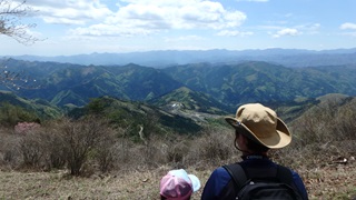 遠くの山まで見渡せる眺望の良い山の上で、登ってきた親子が見下ろしている様子の写真（山で遊ぶのページへリンク）