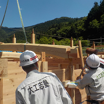 建設中の建物に縄を付けたクレーンで釣り上げた木材を運んでいる様子の写真