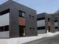 濃いグレーを基調とした壁に正方形の窓が5つ付いているモダン的な四角い建物の本町団地の写真