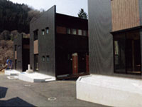 濃いグレーを基調とした壁に正方形の窓が4つ付いている四角いモダン的な建物が横一列に3棟並んでいる「単身用の本町団地」の写真